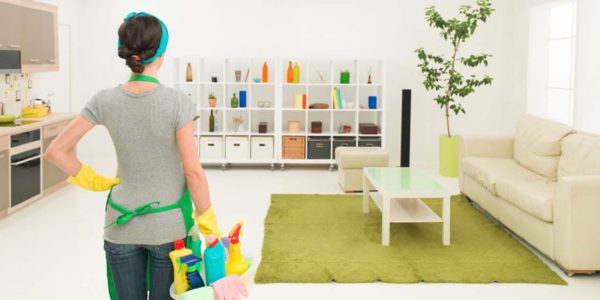 young caucasian woman standing in clean house holding cleaning products, looking at tidy room